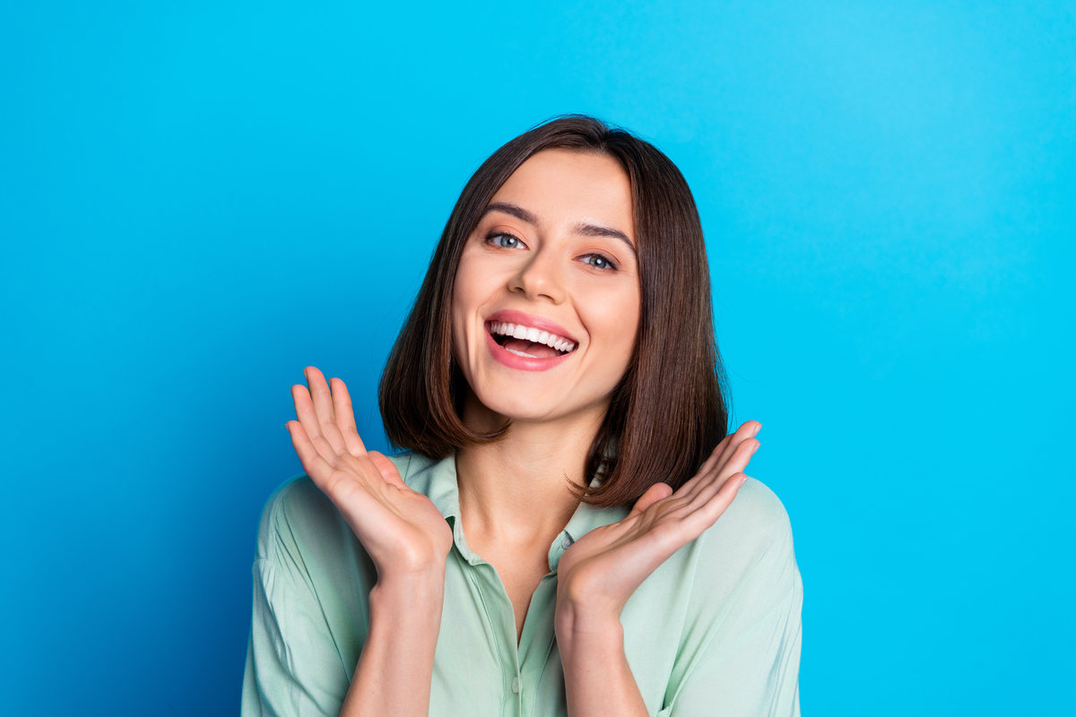 Portrait of gorgeous lovely girl with stylish hair wear teal shirt palms demonstrate white toothy smile isolated on blue color background.