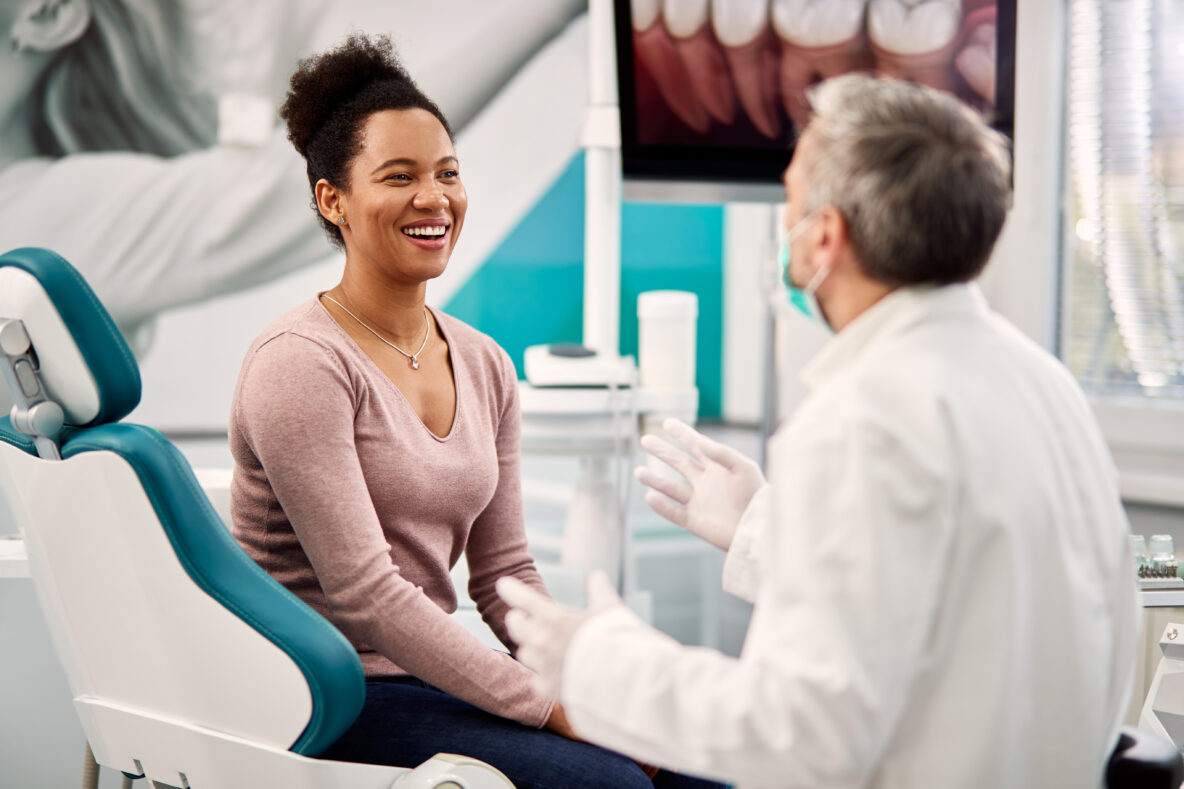 Happy African American woman and her dentist communicating at dentist's office.